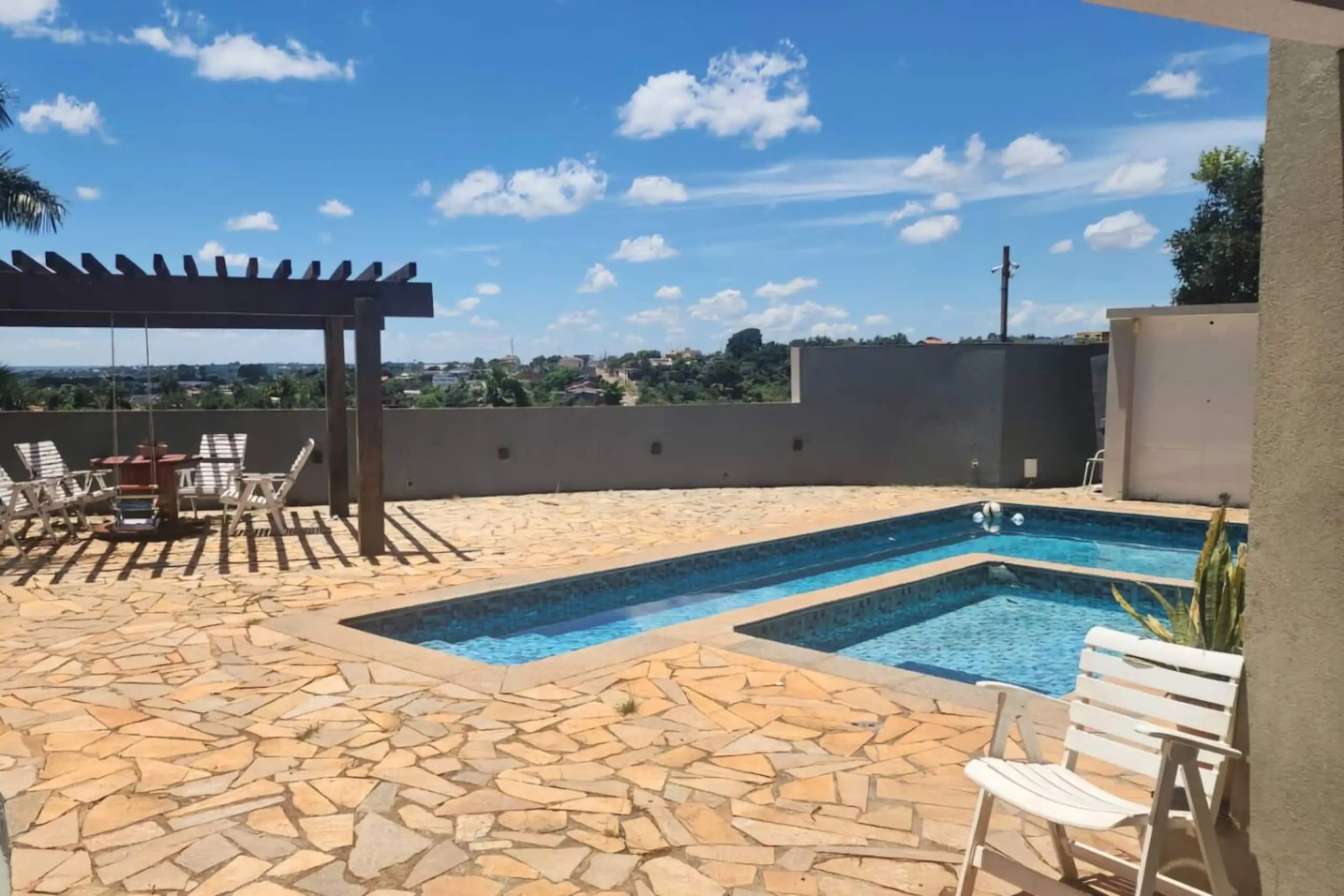 Piscina aquecida com prainha e pergolado, em um dia de céu aberto.