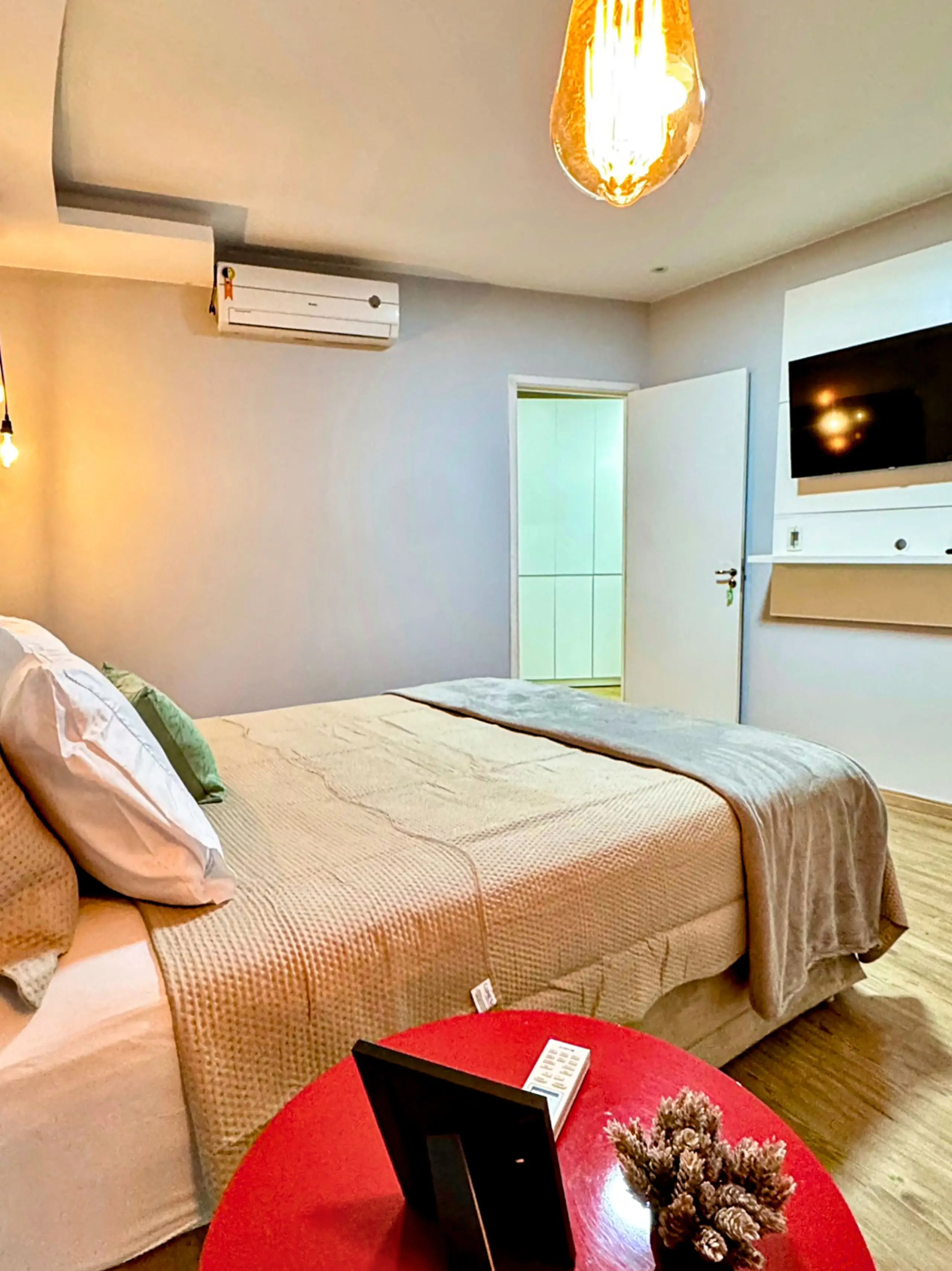 Suíte com cama de casal, ar-condicionado e iluminação suspensa em pontos de luz quente.