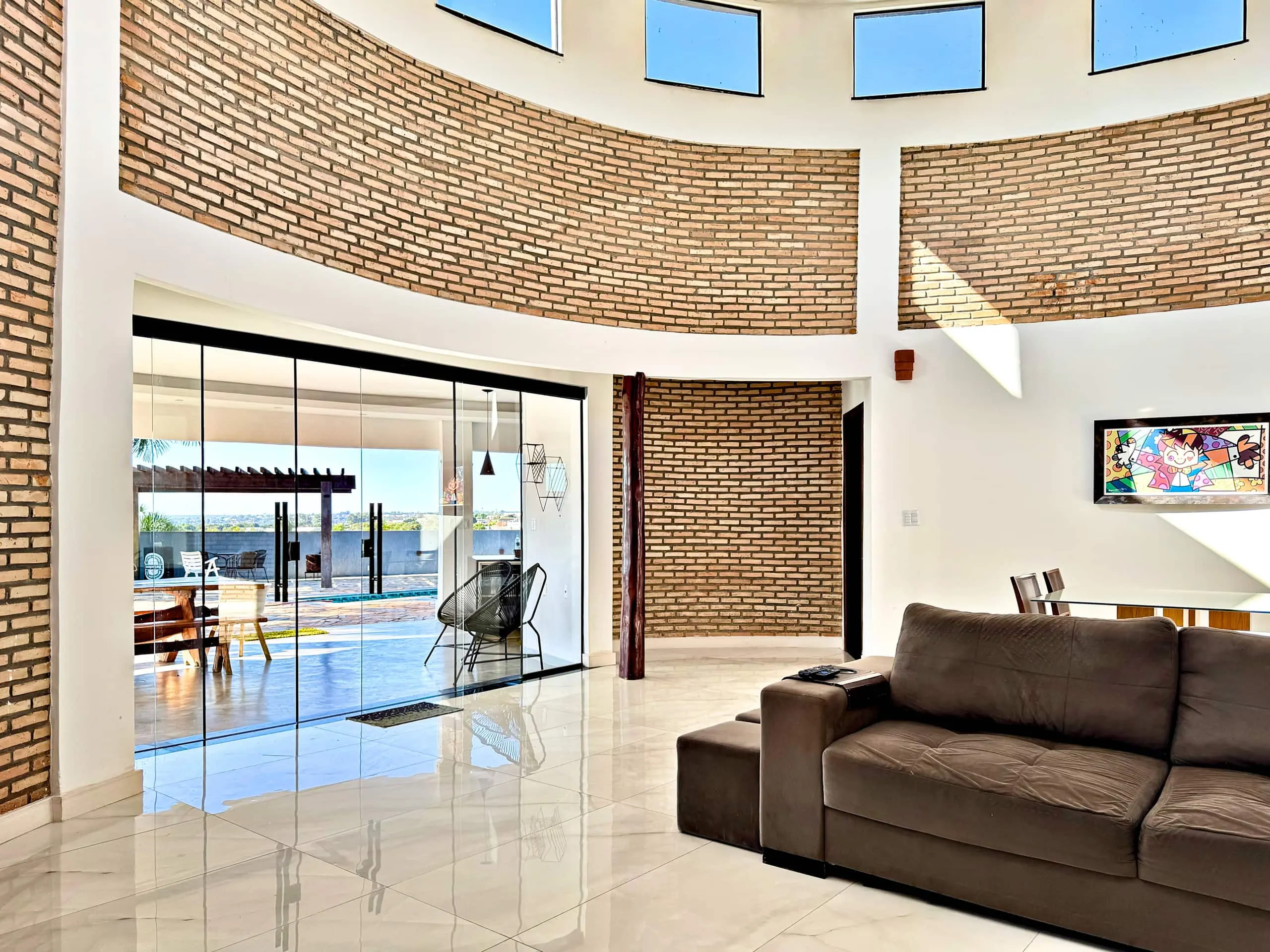Sala de estar ampla, com parede curva de tijolo aparente e piso de mármore.