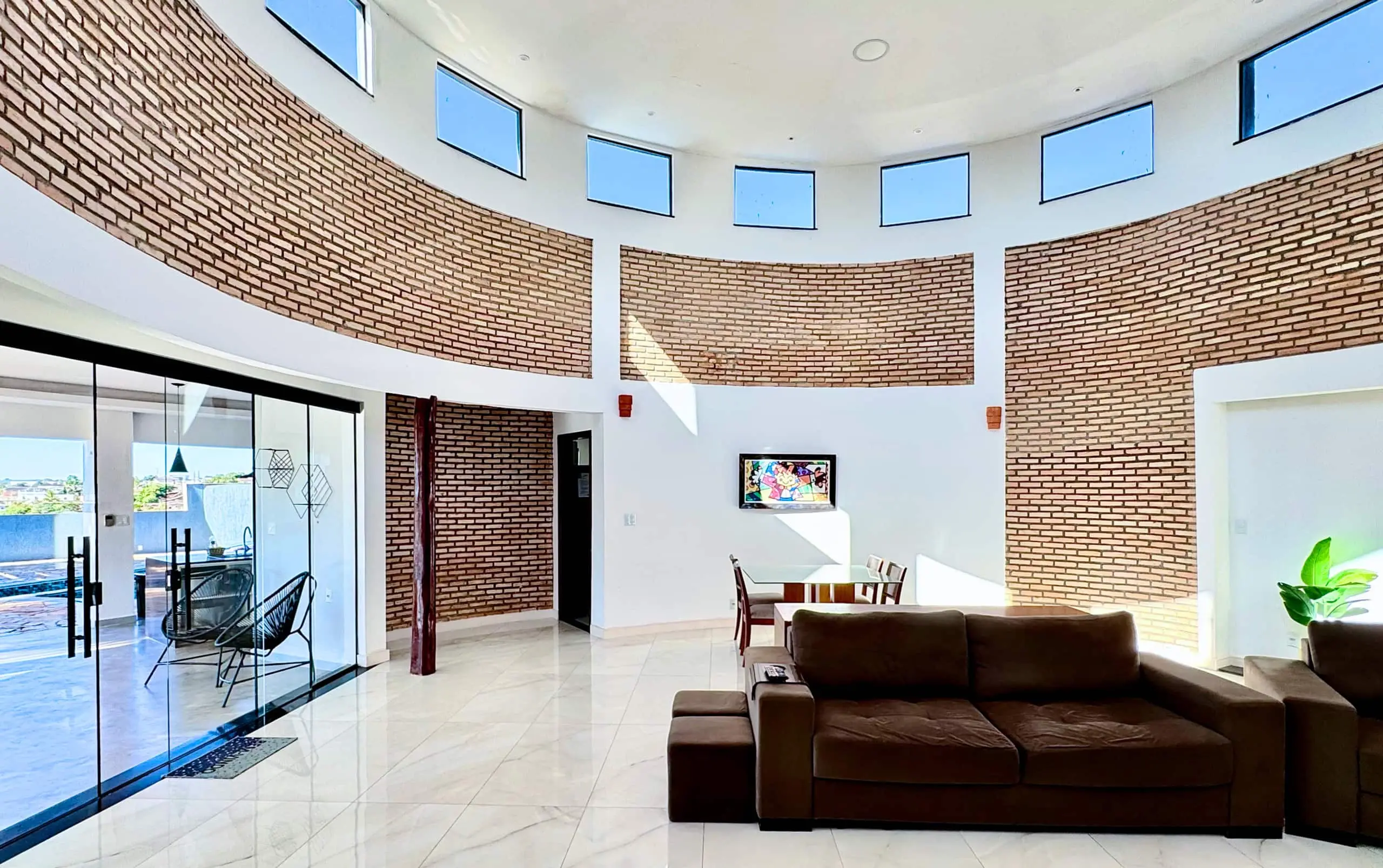 Sala de estar ampla, com parede curva de tijolo aparente e piso de mármore.