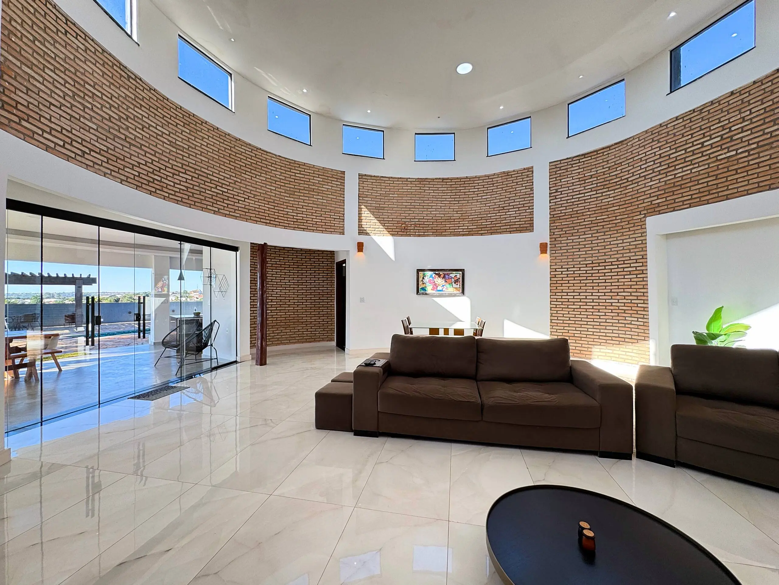 Sala de estar ampla, com parede curva de tijolo aparente e piso de mármore.